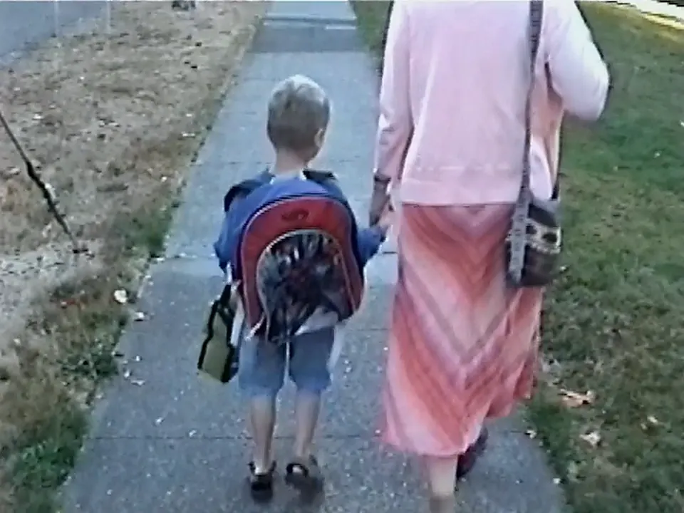 Me and my mom walking to school, seen from behind; I have a big backpack and a lunchbox